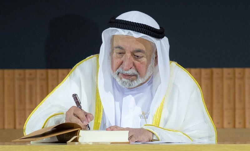 Sultan Muhammad Al Qasimi writing in a bound volume at a formal ceremony
